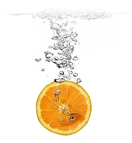 An orange slice being dropped in water to clean it.